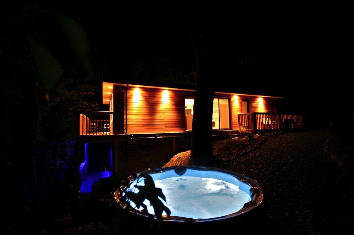 Night-time exterior image of a luxury treehouse with a hot tub lit up